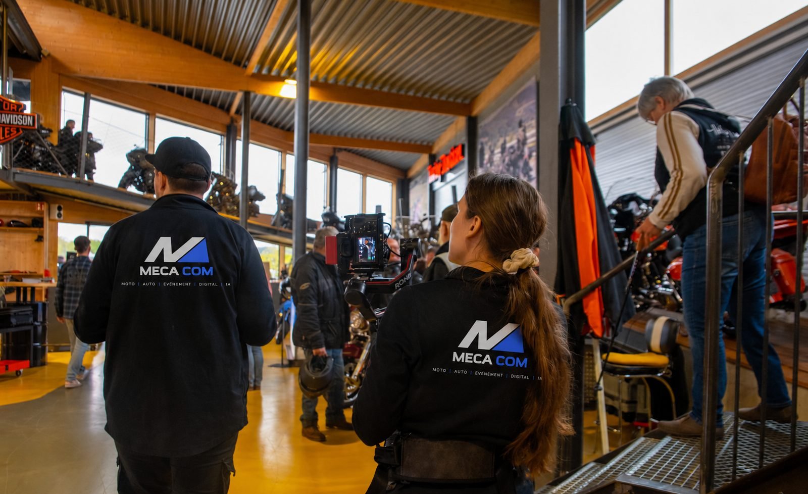 Deux personnes de l’équipe MECA COM, de dos, pendant un tournage dans un showroom moto